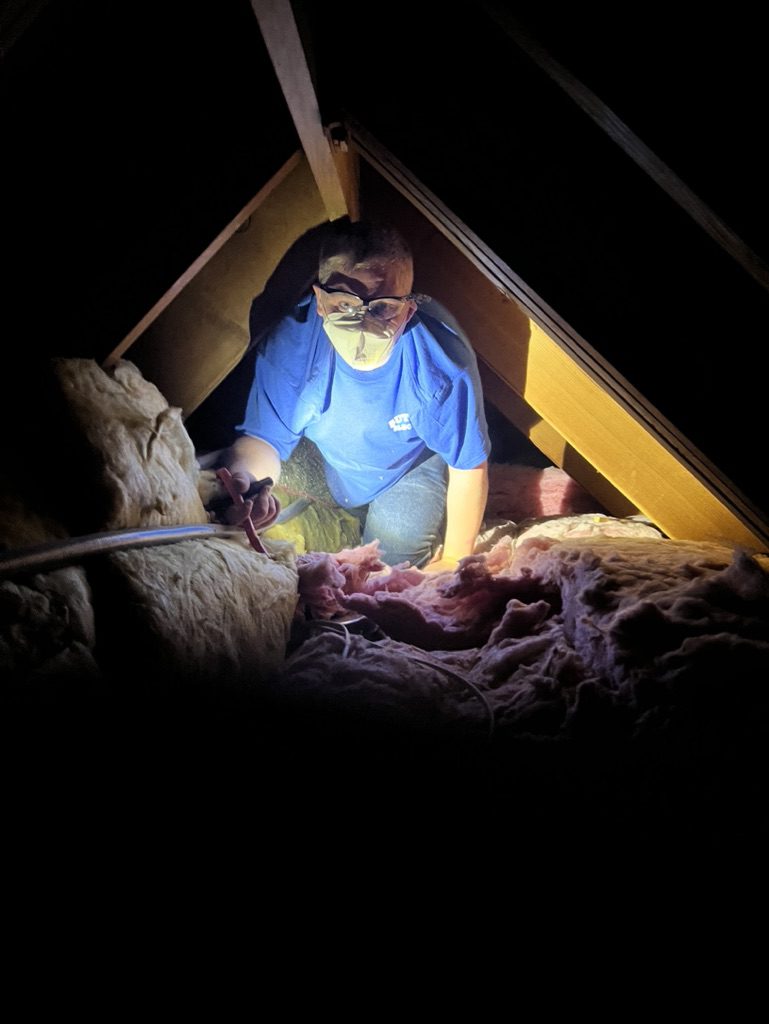 A man in blue shirt working on something inside of an attic.